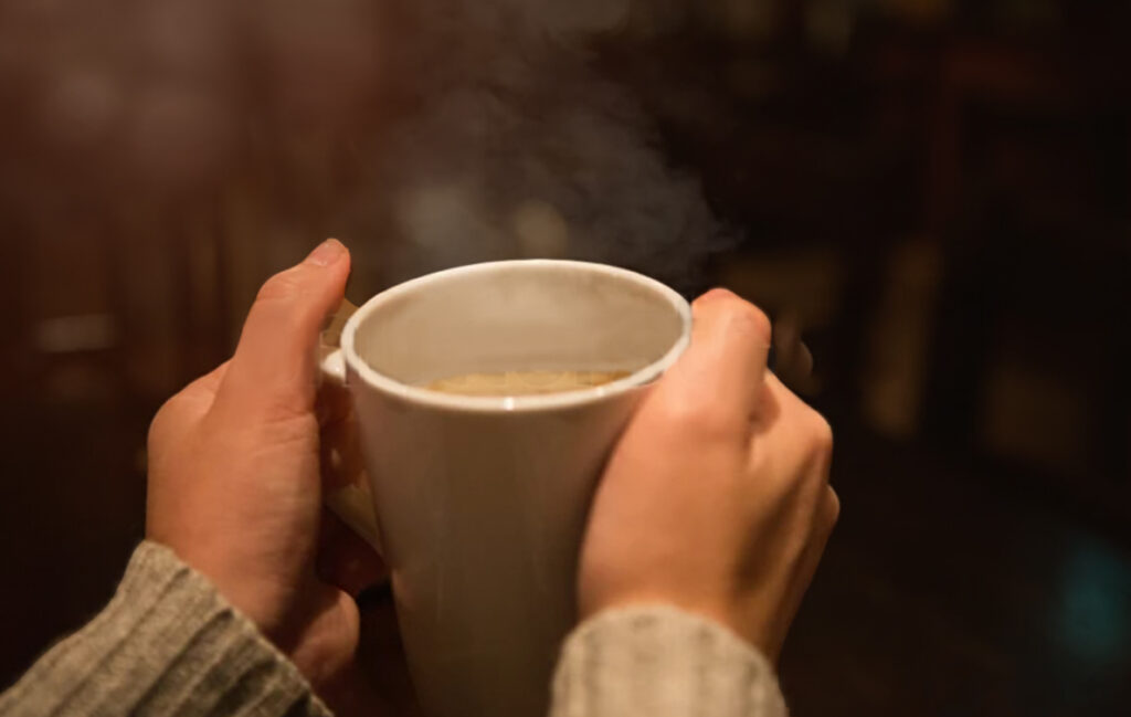 Ricco Coffee – Freshness Guaranteed Steaming Mug Close-up of hands holding a steaming cup of coffee, symbolizing Ricco Coffee’s promise of freshness, quality roasting, and airtight packaging technology