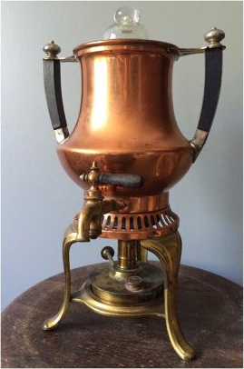 An ornate antique copper stove-top percolator with brass accents and black handles stands elegantly on a wooden surface. Its glass top, a window to the past, and the intricate metalwork reflect the percolator’s rich history, dating back to the late 1800s. This percolator is a symbol of the era when Italian "caffettiera" influenced the art of coffee brewing, serving as a functional piece of history that reminds us of the evolution from simple boiling to the efficient percolating method that became beloved in kitchens until the 1970s.