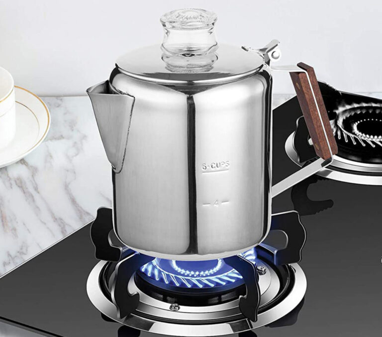A contemporary stainless steel stovetop percolator sits on a modern gas stove, with its glass lid showcasing the brewing process. The polished surface reflects its surroundings, highlighting the blend of traditional brewing methods with modern kitchen aesthetics. This image emphasizes the percolator's suitability for use on various heat sources while also hinting at the importance of manual cleaning to maintain its sleek appearance and functionality.