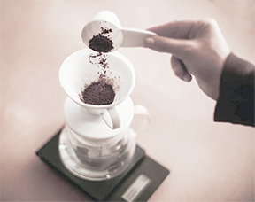 A hand carefully spooning ground coffee into a pour over filter atop a digital scale, a crucial step in ensuring the precise coffee-to-water ratio for a perfectly balanced brew.