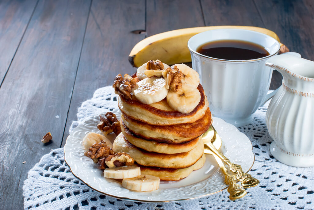 A comforting breakfast setup featuring a tall stack of pancakes with bananas and walnuts, accompanied by a freshly brewed cup of pour-over coffee, inviting you to savor the flavors and aromas of a handcrafted morning delight.