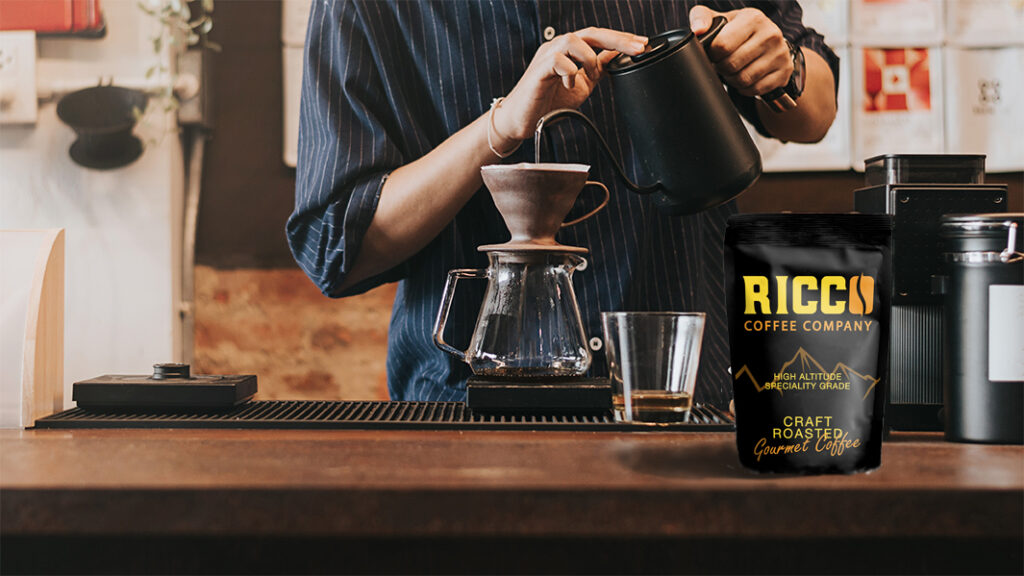 A skilled barista mastering the pour-over brewing technique, delicately pouring water from a black gooseneck kettle over a dripper to extract flavors from specialty-grade coffee beans, with a pack of Ricco Coffee Company’s craft-roasted gourmet coffee on the counter, representing the evolution of clean and consistent light roast profiles.