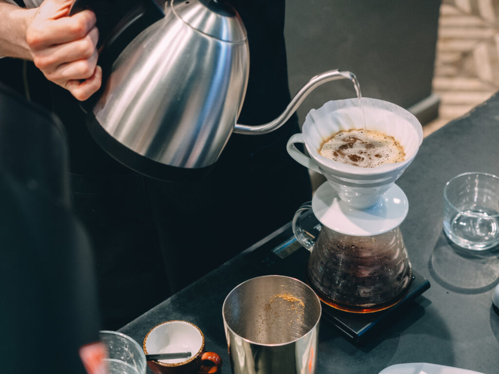 A barista in the process of pour over brewing, pouring water at the ideal temperature over freshly ground coffee for an even and flavorful extraction.